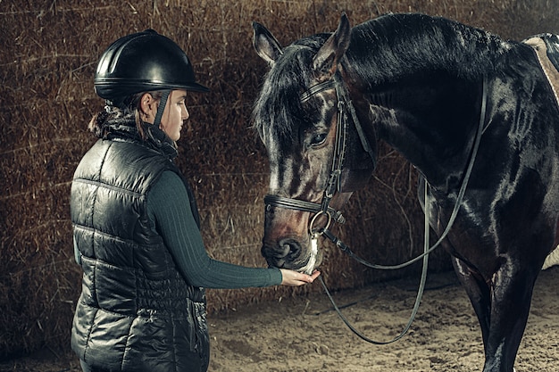 Imagen de feliz hembra de pie cerca de caballo de raza pura