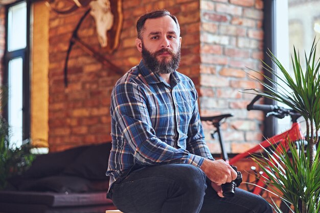 Imagen de un fotógrafo aficionado hipster barbudo tomando fotografías en una habitación con interior tipo loft.