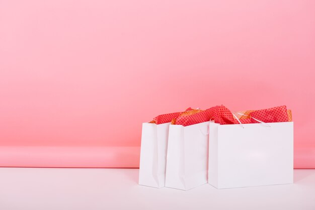 Imagen de grandes bolsas de papel de la tienda con paquetes de regalo de adorno en el interior de pie en el suelo sobre fondo rosa. Alguien ha preparado regalos románticos para el aniversario de la boda dejándolos en la habitación