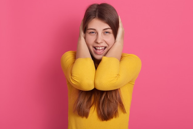 Foto gratuita imagen de una hembra joven divertida, activa y activa abriendo ampliamente la boca, cubriendo sus orejas con las manos, gritando, evitando ruidos fuertes, vistiendo una sudadera amarilla. concepto de emociones