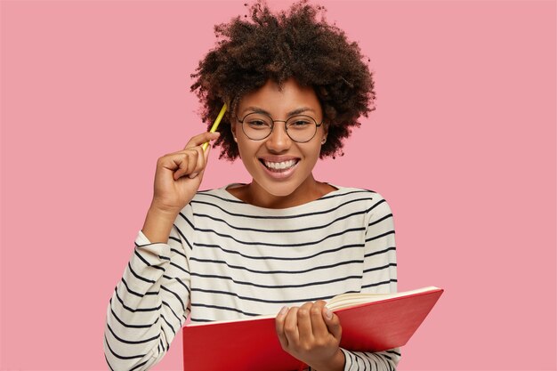 Imagen de la hermosa chica alegre con una gran sonrisa escribe notas en el cuaderno con lápiz