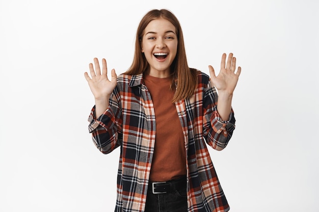 Imagen de una hermosa chica sonriendo amistosamente, agitando las manos para decir hola, hola gesto, dar la bienvenida o saludar a alguien, saludar adiós, de pie contra el fondo blanco