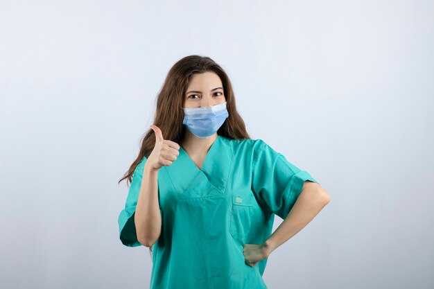 Imagen de una hermosa enfermera en uniforme verde mostrando un pulgar hacia arriba