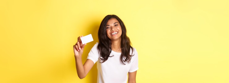 Foto gratuito imagen de una hermosa mujer afroamericana sonriendo feliz mostrando una tarjeta de crédito de pie sobre un fondo amarillo