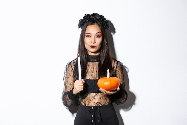 Foto gratuita imagen de hermosa mujer asiática en traje de bruja, sosteniendo una vela encendida y calabaza, celebrando halloween.