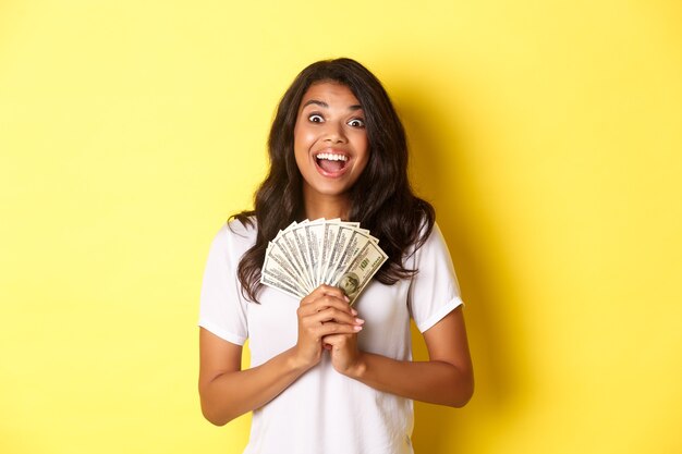 Imagen de la hermosa niña afroamericana emocionada ganando un premio en efectivo y sonriendo sosteniendo efectivo