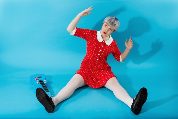 Imagen de hermosa niña dollish con cabello corto violeta claro con vestido rojo sobre pared azul