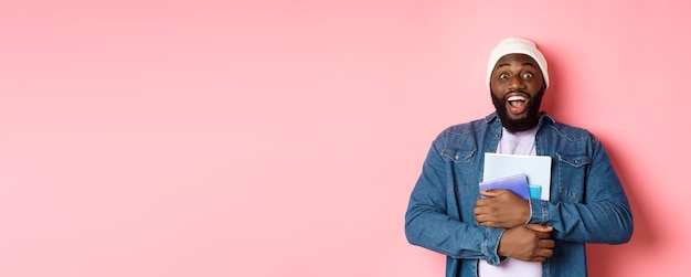 Imagen de un hombre afroamericano adulto sosteniendo cuadernos y sonriendo estudiando en cursos de pie sobre p