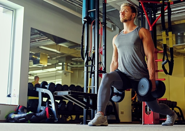 Imagen de un hombre atlético de cuerpo completo haciendo sentadillas con mancuernas en un gimnasio.