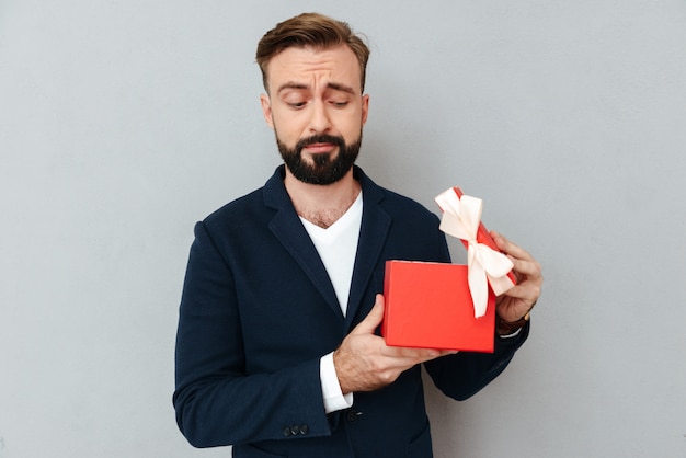 Imagen del hombre barbudo sorprendido en ropa de negocios abriendo regalo