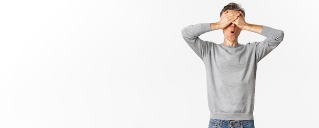 Foto gratuita imagen de un hombre emocionado de mediana edad con un suéter gris que cubre los ojos con las manos y se ve asombrado mientras espera