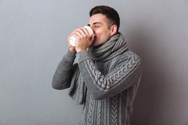 Imagen de hombre enfermo en suéter y bufanda tomando té