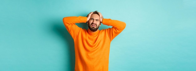 Imagen de un hombre frustrado con suéter naranja cogido de la mano en la cabeza y sintiéndose angustiado de pie anxi