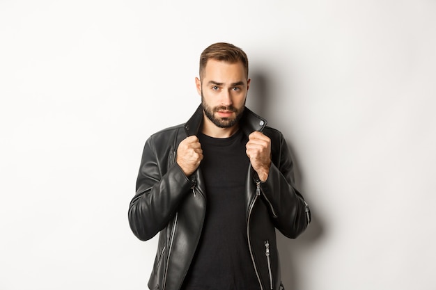 Foto gratuita imagen de hombre guapo y seguro de ponerse la chaqueta de motorista de cuero, de pie