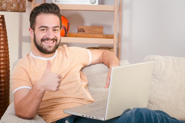 Imagen de hombre independiente feliz mostrando signo bien mientras trabaja en la computadora portátil en casa.