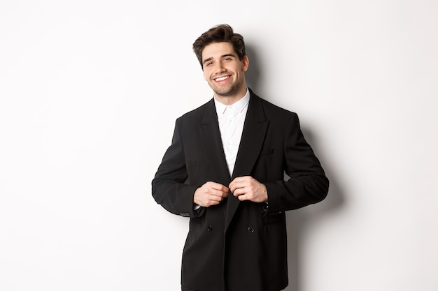 Imagen de hombre de negocios guapo y seguro con barba, chaqueta abotonada y sonriente, de pie contra el fondo blanco.