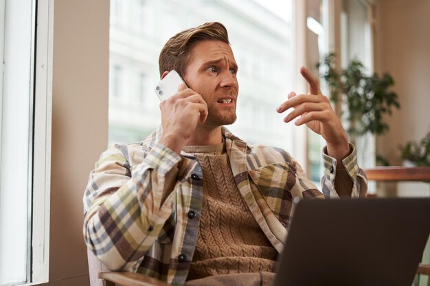 Imagen de un hombre que se siente estresado mientras habla por teléfono un hombre de negocios sentado en un café con una computadora portátil