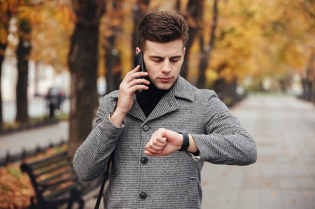 Imagen de un hombre serio hablando por teléfono móvil durante una reunión, verificando el tiempo con el reloj en la mano