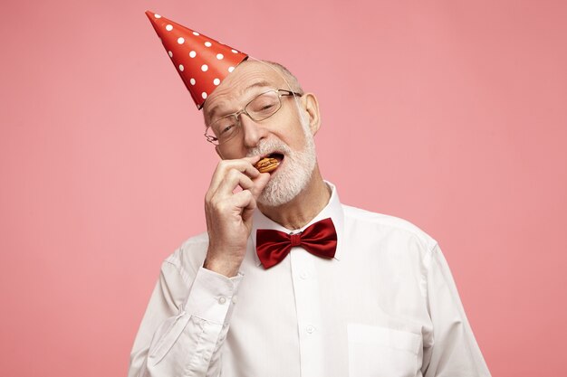 Imagen horizontal de atractivo hombre senior con estilo con barba gris y sombrero de cono