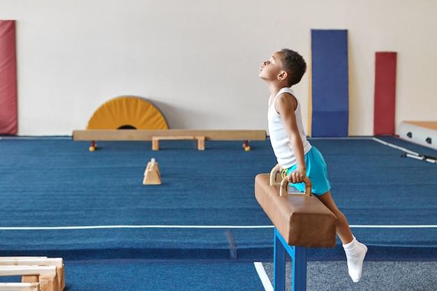 Imagen horizontal del niño gimnasta afroamericano calificado preparándose para la competencia de gimnasia artística