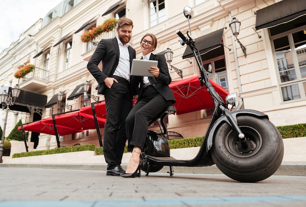 Imagen integral de la feliz pareja de negocios posando cerca de moto