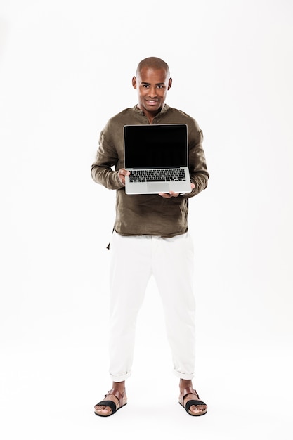 Imagen integral del hombre africano feliz que muestra la pantalla de la computadora portátil en blanco y mirando