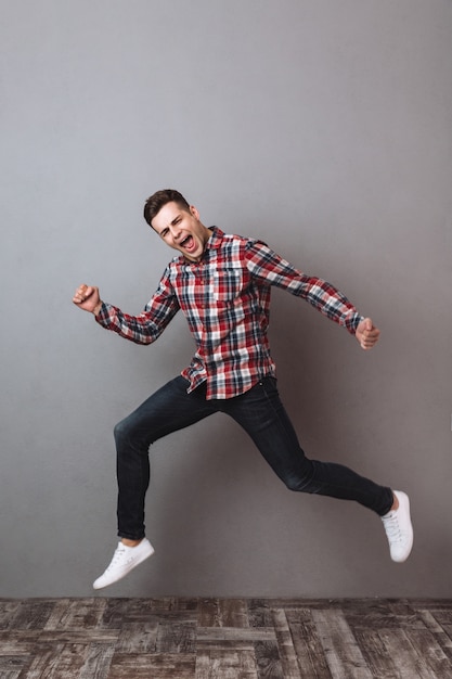 Imagen integral del hombre feliz en camisa y jeans gritando mientras corre y mira