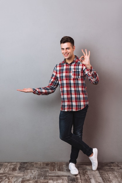 Imagen integral del hombre sonriente en camisa y jeans con copyspace en la palma y mostrando un signo bien mientras mira