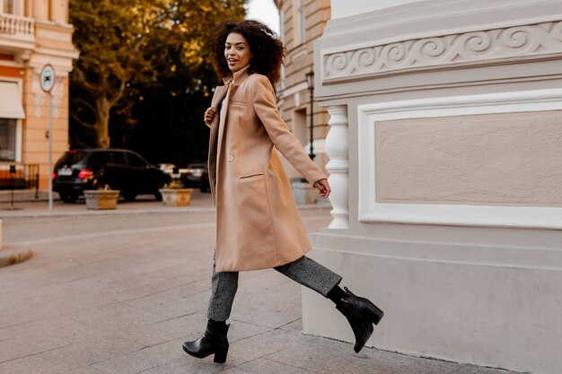 Imagen integral de moda de mujer negra elegante con elegante abrigo beige de lujo y suéter de terciopelo