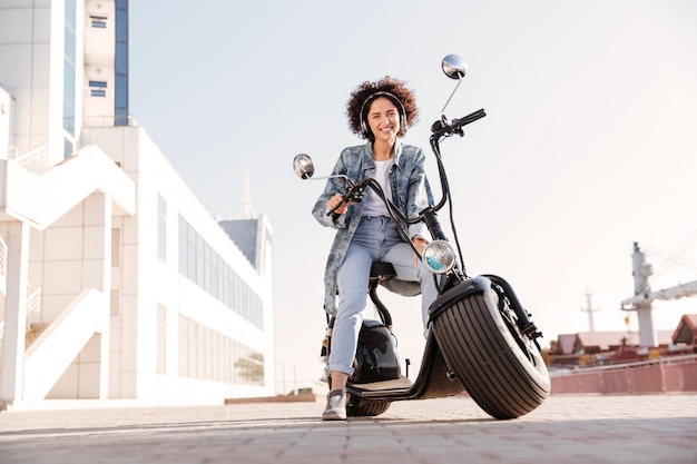 Foto gratuita imagen integral de sonriente mujer rizada sentada en moto