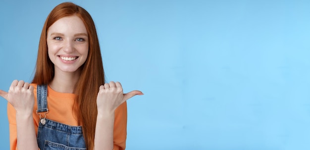 Foto gratuita imagen de interior carismática asertiva feliz sonriente mujer pelirroja camisa naranja mono apuntando