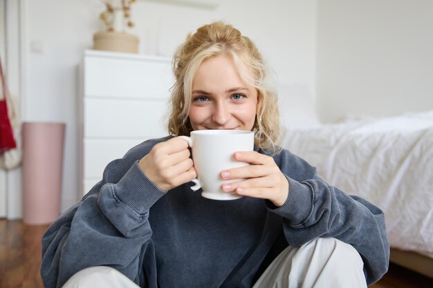 Imagen de una joven adolescente sentada en su dormitorio en el suelo bebiendo una taza de té y disfrutando del día en