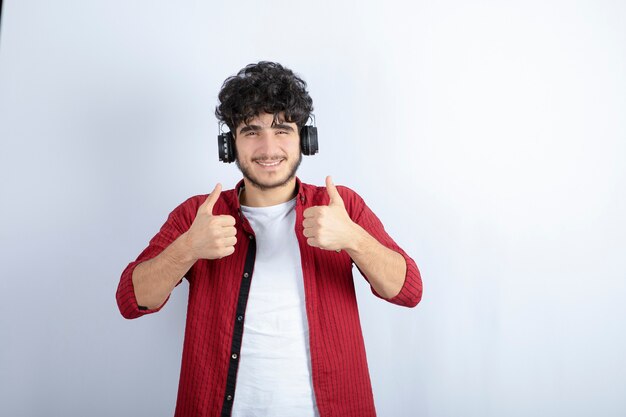 Imagen de un joven apuesto en auriculares escuchando una canción sobre la pared blanca.