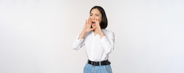 Foto gratuita imagen de una joven asiática llamando a alguien gritando fuerte y buscando de pie contra w