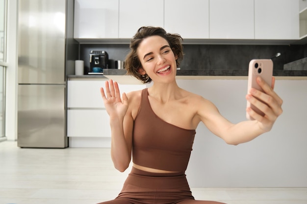 Foto gratuita la imagen de una joven bloguera de fitness graba su entrenamiento en chats en casa en línea mientras hace yoga en bri