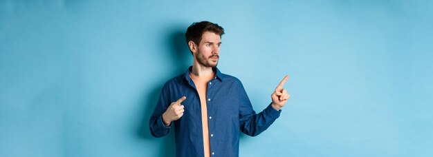 Imagen de un joven caucásico mirando y señalando a un lado mostrando un anuncio de pie en el respaldo azul