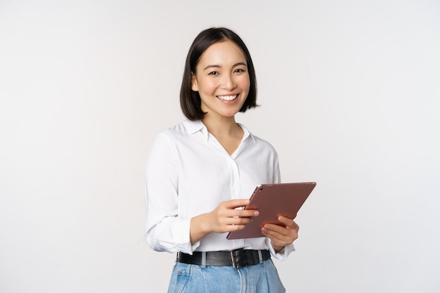 Imagen de una joven directora ejecutiva coreana que trabaja sosteniendo una tableta y sonriendo de pie sobre un fondo blanco