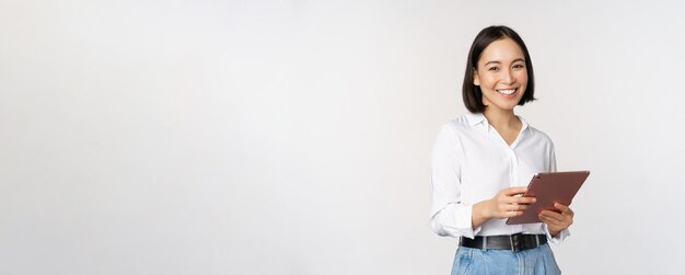 Imagen de una joven directora ejecutiva coreana que trabaja sosteniendo una tableta y sonriendo de pie sobre un fondo blanco