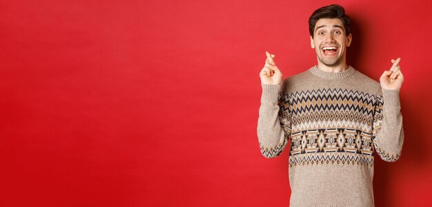 Imagen de un joven emocionado y esperanzado pidiendo deseos vistiendo un suéter de invierno cruzando los dedos para siempre ...