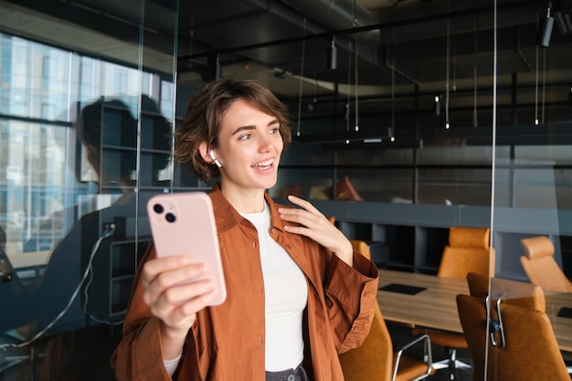 Foto gratuita imagen de una joven empresaria en una oficina parada con un teléfono inteligente hablando en línea se une a una reunión en