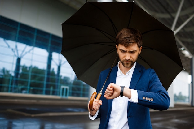 Imagen del joven empresario sosteniendo paraguas y mirando de guardia en la terminal lluviosa