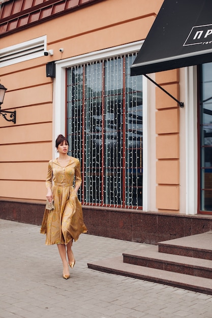 Foto gratuita imagen de joven encantadora mujer caucásica con cabello oscuro en vestido dorado y zapatos dorados muestra diferentes stands cerca del hermoso edificio