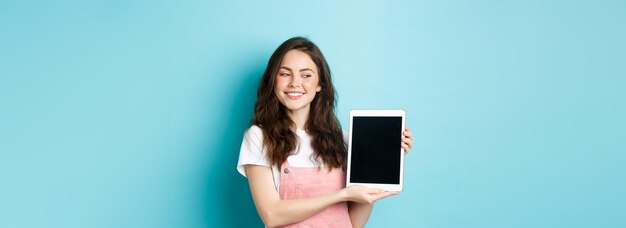 Imagen de una joven feliz mostrando la pantalla de una tableta digital y sonriendo orgullosa mostrando su logotipo en pantalla