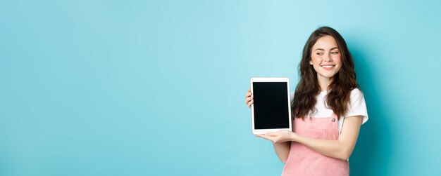 Imagen de una joven feliz mostrando la pantalla de una tableta digital y sonriendo orgullosa mostrando su logotipo en pantalla