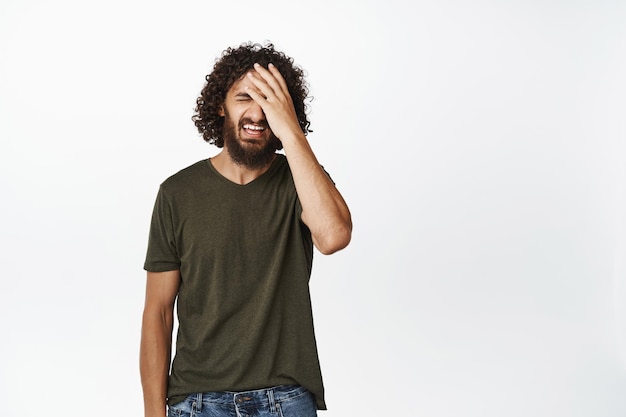 Imagen de un joven frustrado que no se siente molesto haciendo facepalm por arrepentirse de estar decepcionado contra el fondo blanco