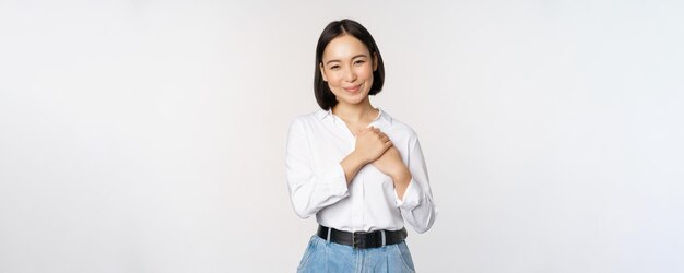 Imagen de una joven y hermosa mujer asiática cariñosa cogida de la mano en el corazón que parece complacida y feliz sonriendo