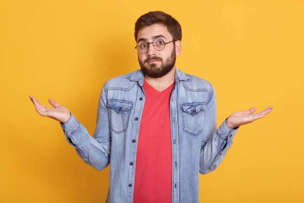 Imagen del joven impotente guapo magnético encogiéndose de hombros, mirando directamente levantando los brazos