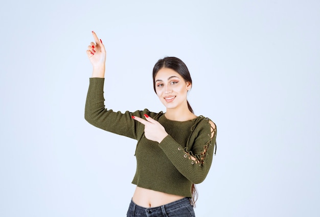 Imagen de una joven modelo de mujer sonriente de pie y apuntando a un lado con los dedos índices