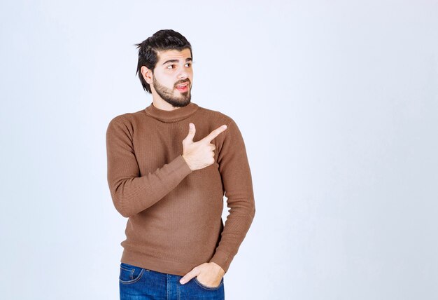 Imagen de un joven modelo sonriente de pie y apuntando hacia arriba con el dedo índice. Foto de alta calidad