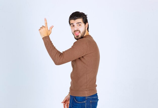 Imagen de un joven modelo sonriente de pie y apuntando hacia arriba con el dedo índice. Foto de alta calidad